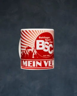 Weiße Kaffeetasse mit rotem BSC-Logo, Fansilhouetten und Schriftzug